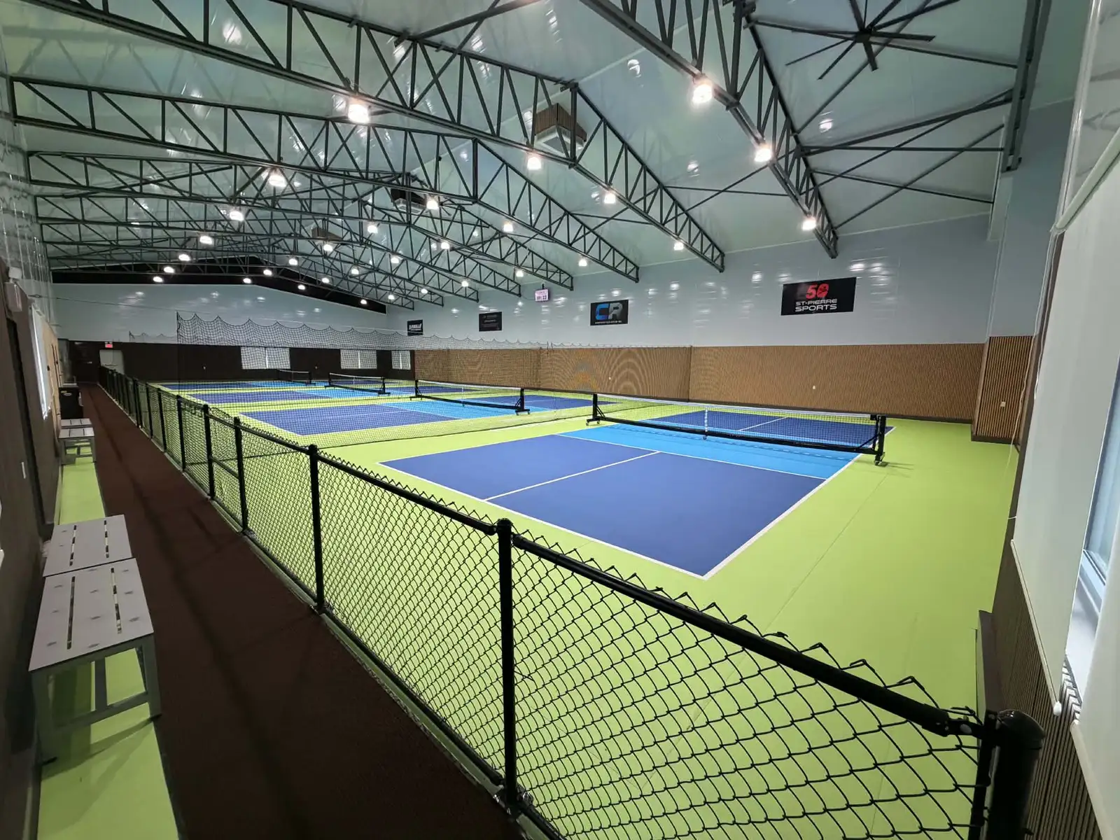 Vue en plongée des quatre terrains de pickleball intérieurs depuis la passerelle