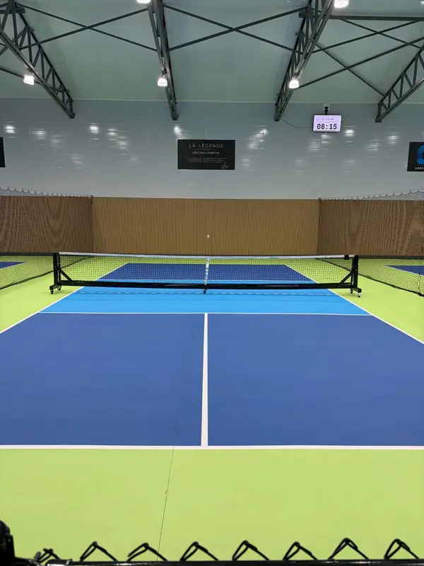 Terrain de pickleball intérieur, enseigne La Légende – Léo Guillemette au mur du fond, écran de compte à rebours en haut à droite