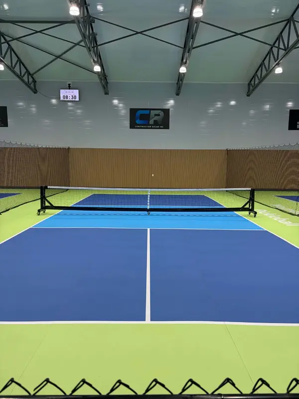 Terrain de pickleball intérieur, enseigne Construction Récam au mur du fond, écran de compte à rebours en haut à gauche